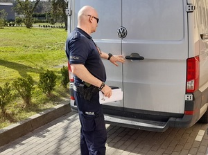 policjant służby konwojowej zamyka tylne drzwi nieoznakowanego radiowozu. W ręce trzyma dokumenty