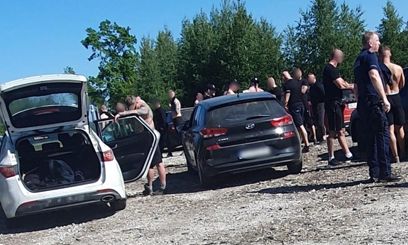 grupa pseudokibiców stojąca przy samochodach