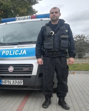 POLICJANT STOI PRZY RADIOWOZIE OZNAKOWANYM