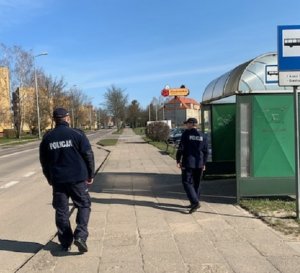 chodnikiem, obok przystanku autobusowego, idą dwaj umundurowani policjanci