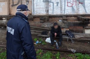 przy starej nieczynnej rampie kolejowej siedzi mężczyzna. Przed nim stoi umundurowany policjant, skierowany tyłem do obiektywu