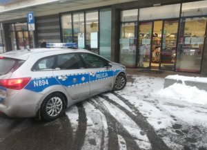 zimowa pora. Przed wejściem do drogerii stoi oznakowany radiowóz