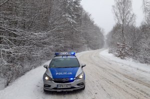 na zaśnieżonej drodze stoi oznakowany radiowóz z włączonymi sygnałami świetlnymi