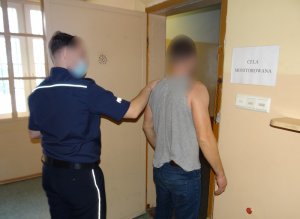 przed wejściem do celi w pomieszczeniu dla osób zatrzymanych stoi skierowany tyłem do obiektywu mężczyzna. Za nim znajduje się umundurowany policjant, który wprowadza go do celi