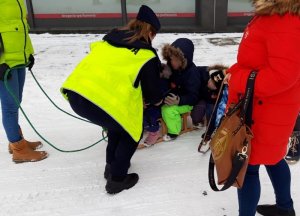 umundurowana policjantka w kamizelce odblaskowej przekazuje dwójce dzieci siedzących na sankach elementy odblaskowe