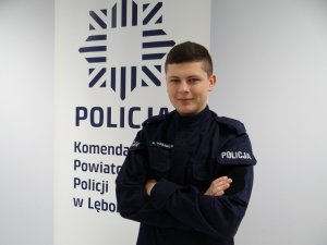 na tle logo policji i napisu komenda powiatowa policji w lęborku stoi umundurowany policjant w stopniu posterunkowego