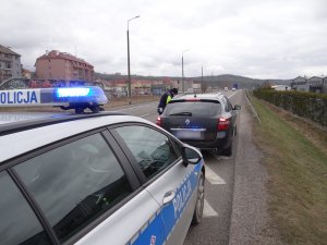 droga krajowa nr 6 w Lęborku. Na poboczu drogi stoi czarny renault laguna. Przed nim znajduje się radiowóz policyjny z włączonymi sygnałami świetlnymi. Przy renault od strony kierowcy stoi umundurowany policjant ruchu drogowego w kamizelce odblaskowej