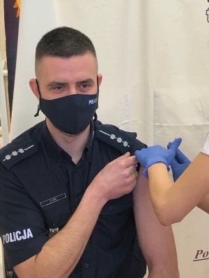 pielęgniarka wstrzykuje w ramię umundurowanego policjanta dawkę szczepionki