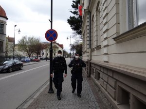 Dwaj umundurowani policjanci w maseczkach ochronnych na twarzach patrolują ulicę Armii Krajowej w Lęborku