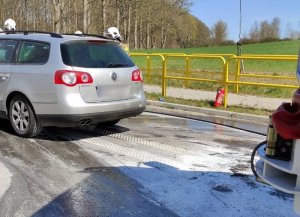 na poboczu drogi w214 znajduje się volkswagen passat. Droga jest pokryta pianą z gaśnicy. Przy aucie stoją strażacy