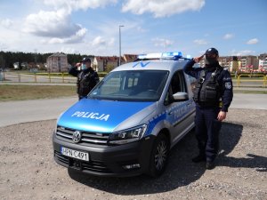 na parkingu w pobliżu stadionu miejskiego, umundurowani policjanci służby patrolowej, stojąc przy radiowozie i salutując, oddają hołd zmarłemu koledze