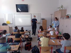 klasa szkolna. Policjantka w maseczce ochronnej na twarzy prowadzi zajęcia z uczniami pierwszej klasy