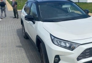 fragment białej toyoty rav4. Za pojazdem stoją dwaj nieumundurowani policjanci