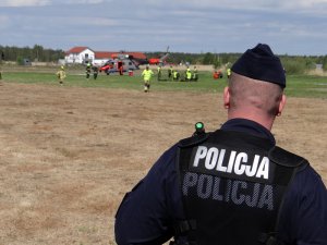 umundurowany policjant oddziałów prewencji obserwuje przebieg ćwiczeń wojskowych do których wykorzystano śmigłowiec