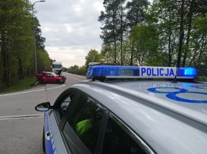 droga K6 przy wjeździe do Lęborka od strony Słupska. Na poboczu po lewej stronie drogi znajduje się czerwone osobowe renault z podniesioną maską. Tył samochodu jest wgnieciony. Za tym pojazdem stoi ciężarowy MAN. Na pierwszym planie zdjęcia widoczny fragment oznakowanego radiowozu z włączonymi sygnałami błyskowymi