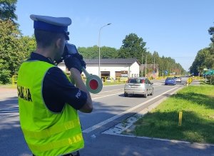 Policjant ruchu drogowego stojący przy drodze dokonuje pomiaru prędkości