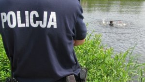 policjant stoi przy jeziorze, w którym znajduje się człowiek