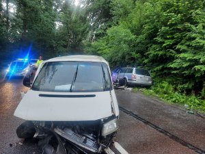 miejsce wypaku drogowego. Na pierwszym planie znajduje się ustawiony na środku drogi vw caravelle z uszkodzonym, wgniecionym przodem. Za nim, po prawej stronie drogi, na poboczu znajduje się vw passat z uszkodzonym bokiem. Za caravelle stoi strażak, a za nim radiowóz policyjny z włączonymi sygnałami błyskowymi