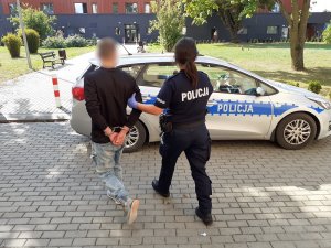 umundurowana policjantka prowadzi skutego kajdankami mężczyznę w kierunku radiowozu