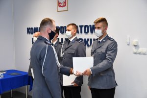 w auli lęborskiej komendy policji komendant wręcza akty mianowania ustawionym w szeregu policjantom