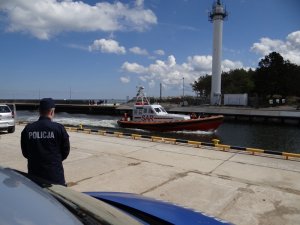 umundurowany policjant stoi przy kanale portowym i obserwuje przepływającą łódź motorową ratownictwa morskiego