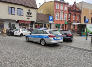 centrum miasta w Lęborku. Na placu pokoju obok zaparkowanych pojazdów stoi oznakowany policyjny radiowóz z włączonymi sygnałami błyskowymi