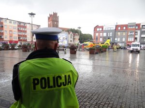 policjant ruchu drogowego zabezpiecza miejsce gdzie wylądował śmigłowiec pogotowia ratunkowego. Obok śmigłowca znajduje się karetka pogotowia