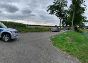 miejsce wypadku drogowego. W poprzek drogi na jezdni leży na dachu audi. Auto ma liczne wgniecenia i pęknięcia karoserii. Przed nim znajduje się nieoznakowany radiowóz, jeszcze wcześniej przy skrzyżowaniu stoi oznakowany radiowóz