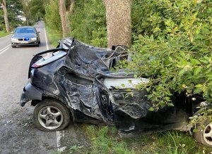 na poboczu drogi znajduje się całkowicie rozbity o drzewo samochód. W tle widać na drodze nieoznakowany radiowóz