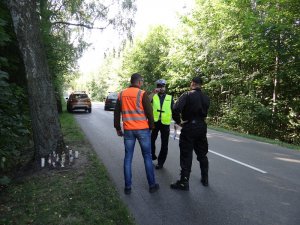 na drodze stoją policjant ruchu drogowego oraz przedstawiciel straży pożarnej i zarządu dróg wojewódzkich prowadząc rozmowę