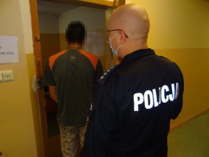 W otwartych drzwiach do celi stoi zatrzymany mężczyzna. Za nim znajduje się policjant służby dyżurnej