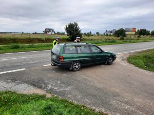 policjant i policjantka z drogówki stoją przy osobowym oplu, zatrzymanym do kontroli