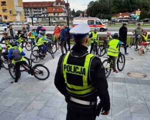 na placu przed dworcem PKP wśród dzieci na rowerach stoi policjant ruchu drogowego