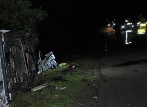 pora wieczorowa. Miejsce wypadku. W rowie po lewej stronie drogi leży przewrócony na bok samochód. Na jezdni stoją się funkcjonariusze i pojazdy służb ratunkowych