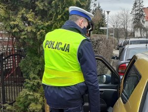 policjant ruchu drogowego stoi przy otwartych drzwiach samochodu osobowego