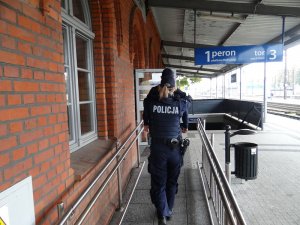 dwoje umundurowanych policjantów idzie w kierunku wejścia do budynku dworca PKP