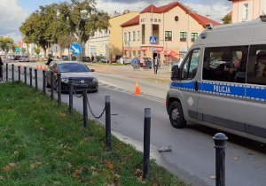 miejsce wypadku drogowego odgrodzone z jednej strony taśmą, z drugiej policyjnym radiowozem. Za przejściem dla pieszych stoi volkswagen uczestniczący w wypadku. Za nim stoją dwaj policjanci ruchu drogowego