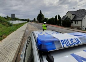 policjant ruchu drogowego stoi przed oznakowanym radiowozem kontrolując ruch na drodze