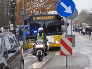 policjant na motocyklu jedzie przed autobusem wiozącym pasażerów na cmentarz