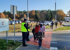 na drodze prowadzącej do cmentarza przy przejściu dla pieszych policjant i policjantka z ruchu drogowego rozdają pieszym odblaski