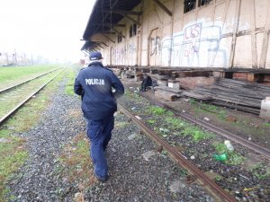 umundurowany policjant idzie wzdłuż torów kolejowych przy starej wyładowni, w kierunku siedzącego tam mężczyzny