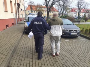 policjant służby konwojowej prowadzi zatrzymanego mężczyznę w kierunku radiowozu