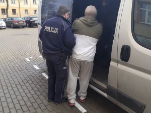 policjant służby konwojowej wprowadza zatrzymanego mężczyznę do nieoznakowanego radiowozu