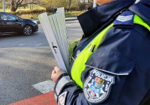 przy jezdni stoi policjantka ruchu drogowego z naręczem opasek odblaskowych