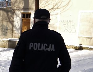 zimową porą umundurowany policjant stoi przed opuszczonym budynkiem