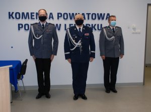 przy ścianie, pod napisem komenda powiatowa policji w Lęborku stoją obok siebie odchodzący komendant, komendant wojewódzki policji w Gdańsku oraz nowo mianowany komendant