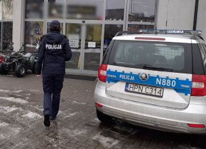 umundurowana policjantka idzie w stronę wejścia do salonu sportowego. Przed salonem zaparkowany jest oznakowany radiowóz