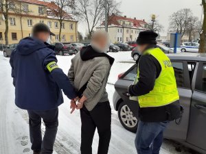 dwaj nieumundurowani policjanci wprowadzają do nieoznakowanego radiowozu mężczyznę skutego kajdankami