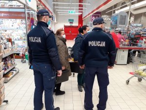 w sklepie wielkopowierzchniowym przed liniami kas stoją dwaj umundurowani policjanci i dwie pracownice sanepidu