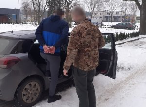 nieumundurowany policjant wprowadza do nieoznakowanego radiowozu mężczyznę skutego kajdankami